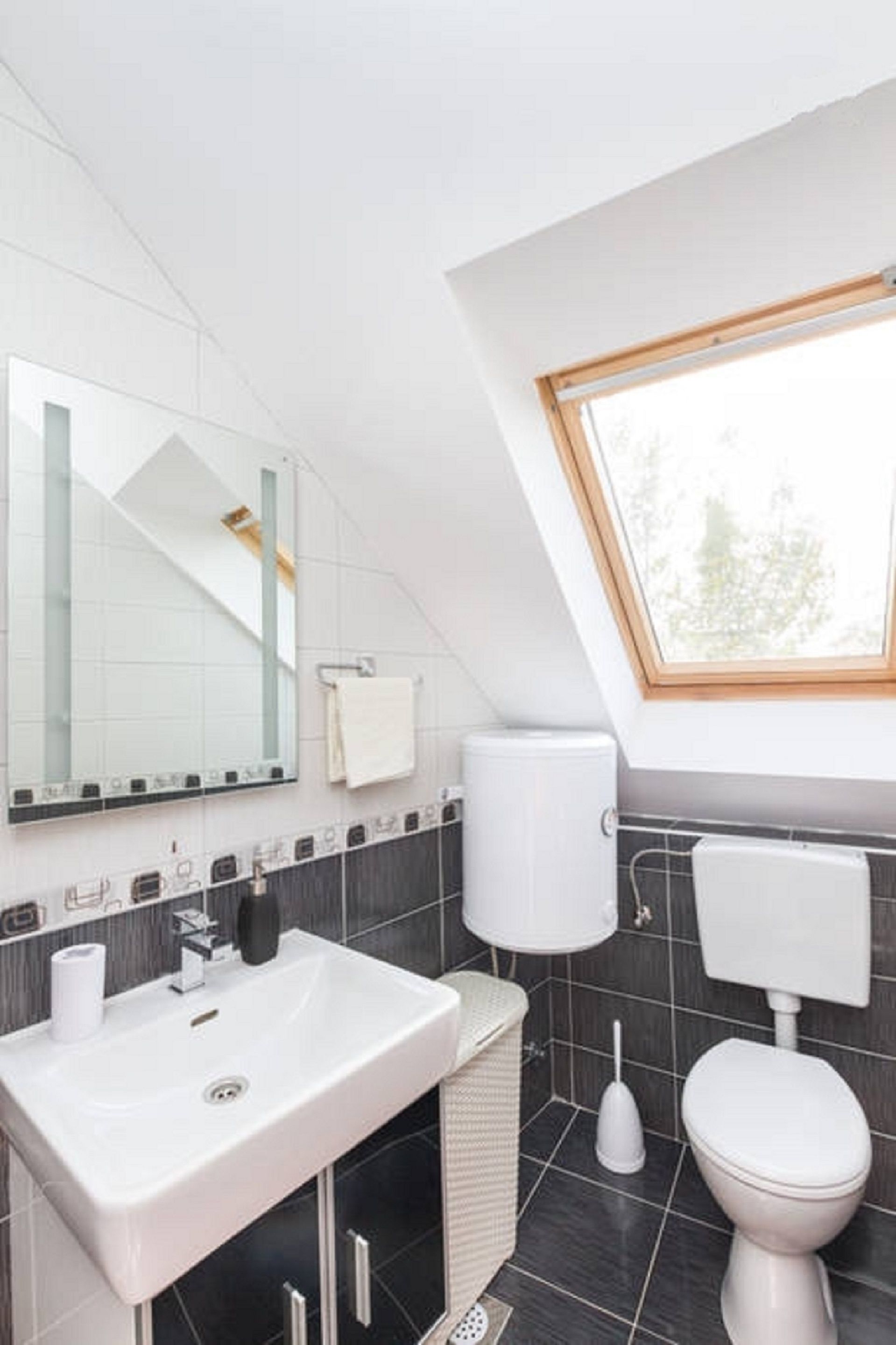 A modern bathroom with a skylight, a white sink, a toilet, and a mirror.