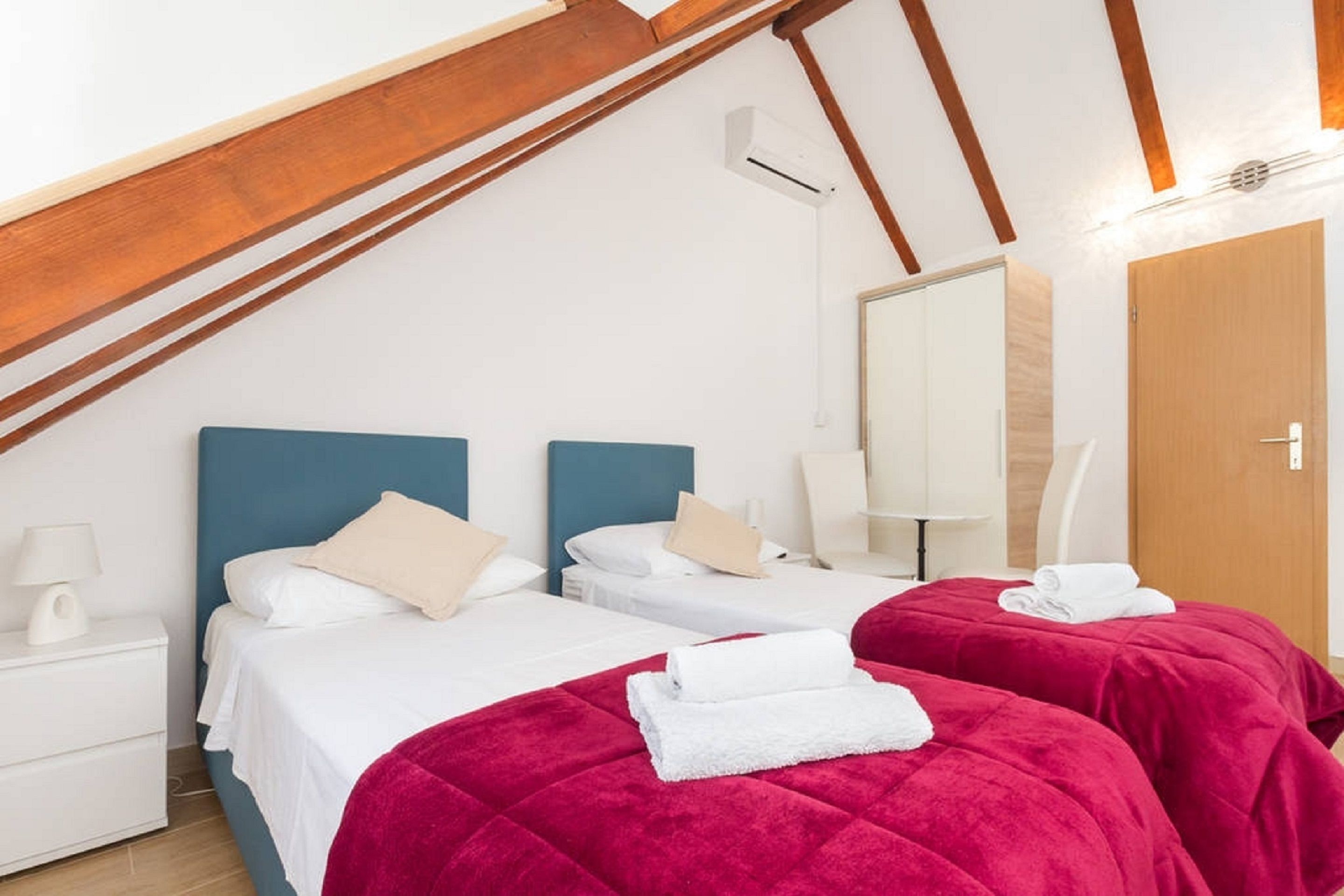 Ein Hotelzimmer mit zwei Betten, einer Holzbalkendecke, einer Klimaanlage, einem Spiegel und einer Holztür.