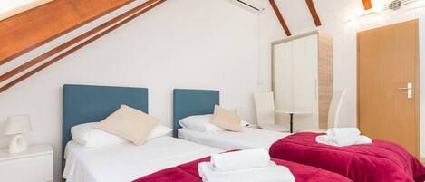 A hotel room with two beds, a wooden ceiling, an air conditioning unit, a mirror, and a wooden door.