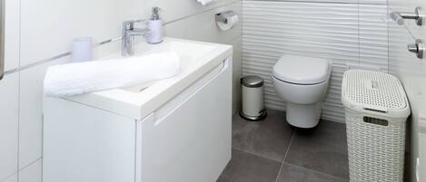 Et moderne badeværelse med et hvidt håndvaskarrangement, spejl og toilet.