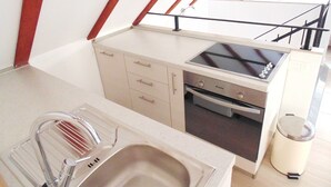 Cocina compacta con lavamanos, estufa y horno, un cubo de basura y un balcón con barandilla.