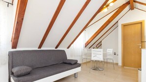 Un loft moderno con techo inclinado, un sofá gris, un comedor con sillas blancas y una puerta de madera.