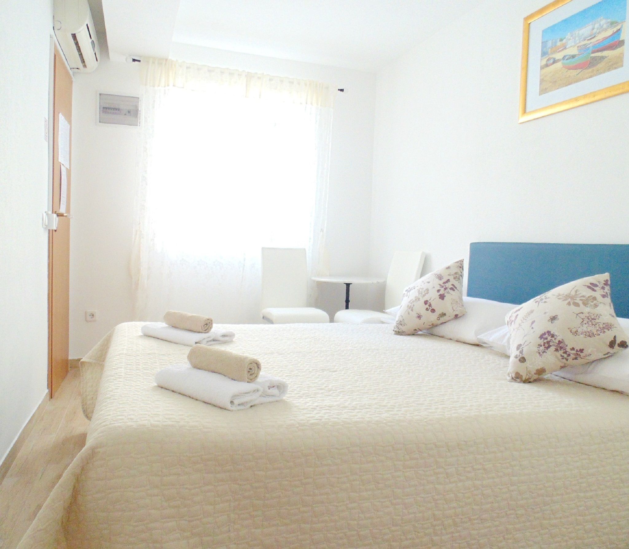 A neatly made bed with rolled towels, a bedside table, a lamp, and a framed picture on the wall.