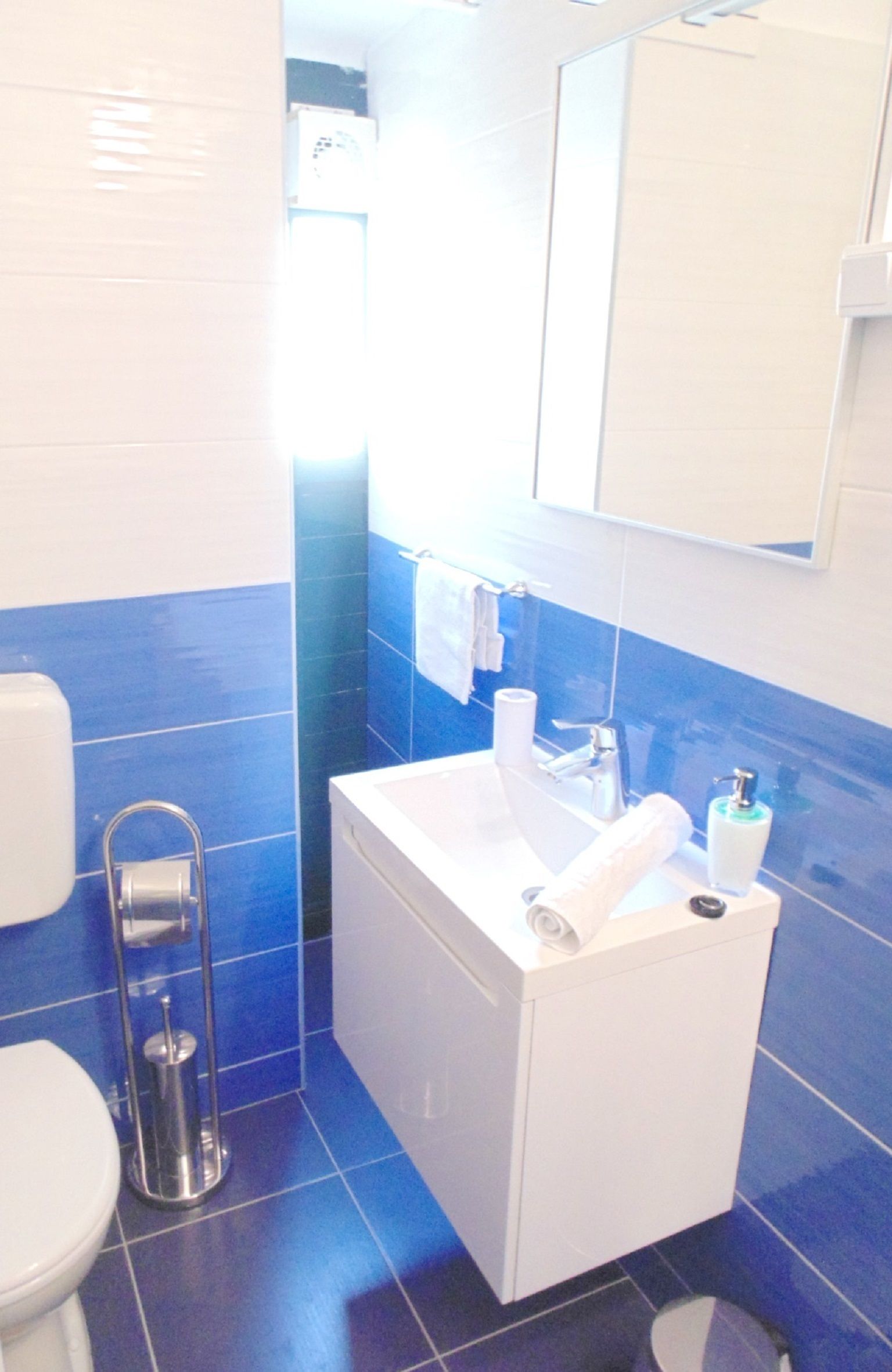 Een badkamer met een witte wasbak, blauwe tegels, een toilet en een spiegel boven de wasbak.