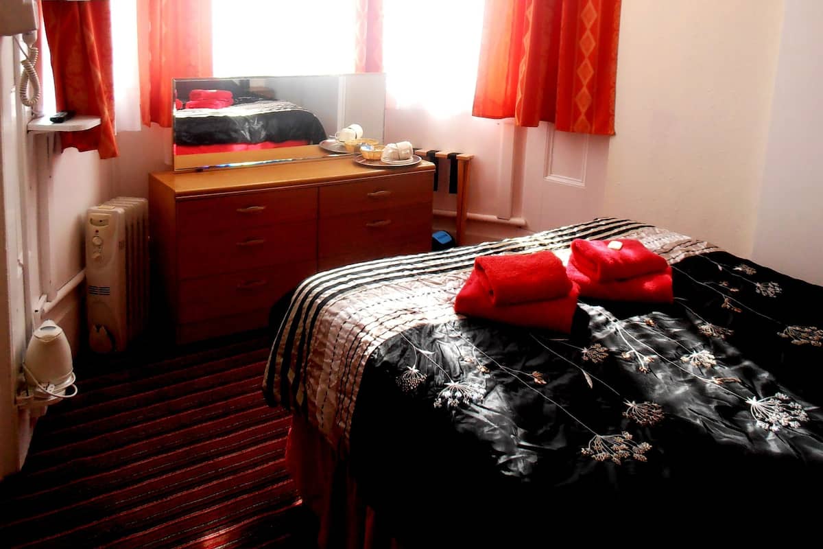Quarto de hotel com cama, escrivaninha, cadeira, televisão e janela com cortinas.