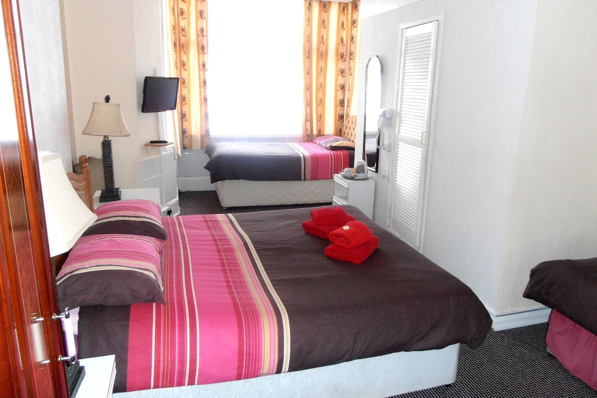 Quarto de hotel com duas camas, televisão, espelho e janela com cortinas.