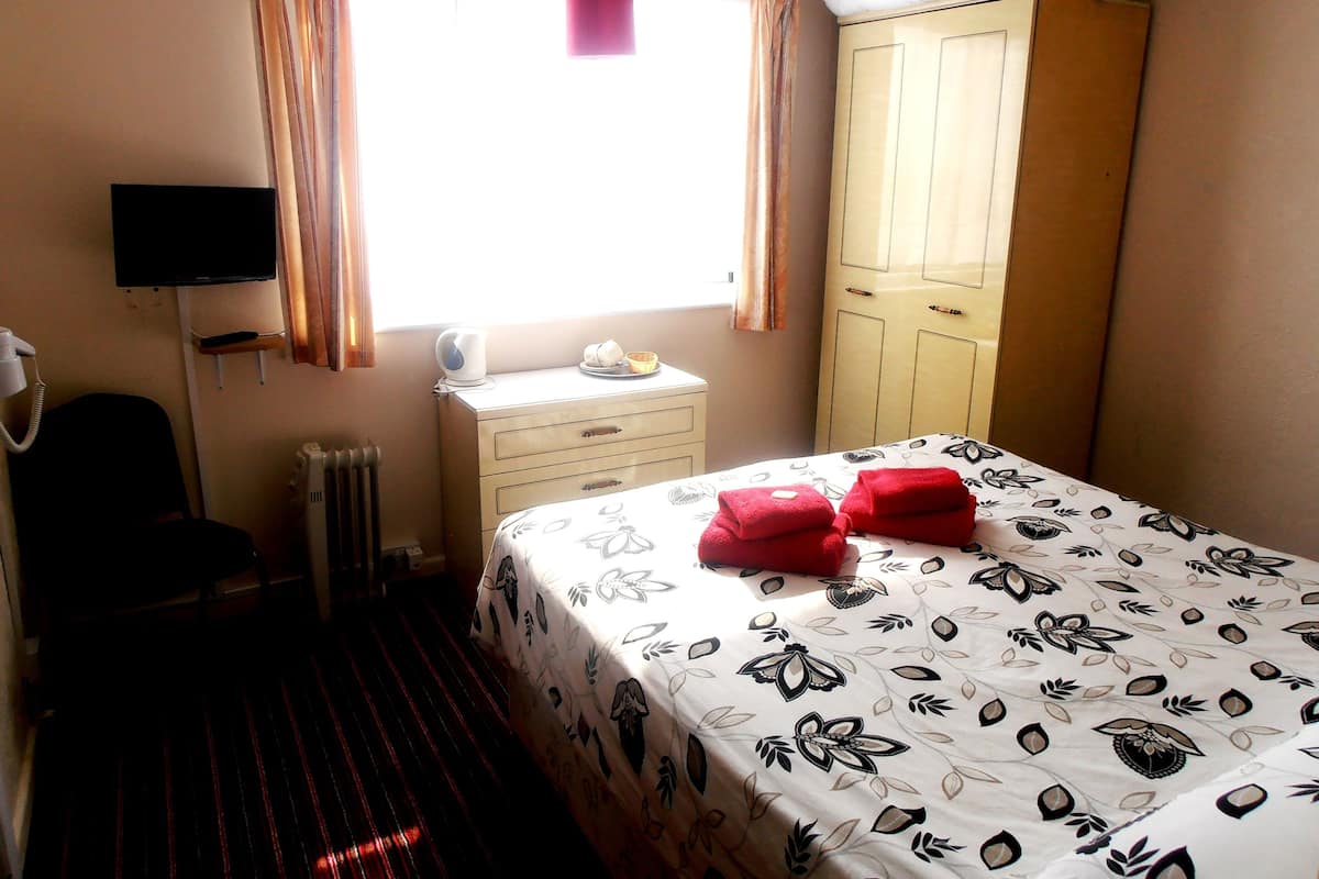 Quarto de hotel com cama, guarda-roupa, mesa de cabeceira com chaleira, telefone e janela com cortinas.