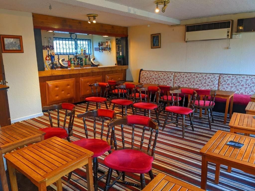 A bar area with stools and a counter, a seating area with red upholstered chairs and tables, and a patterned carpet.