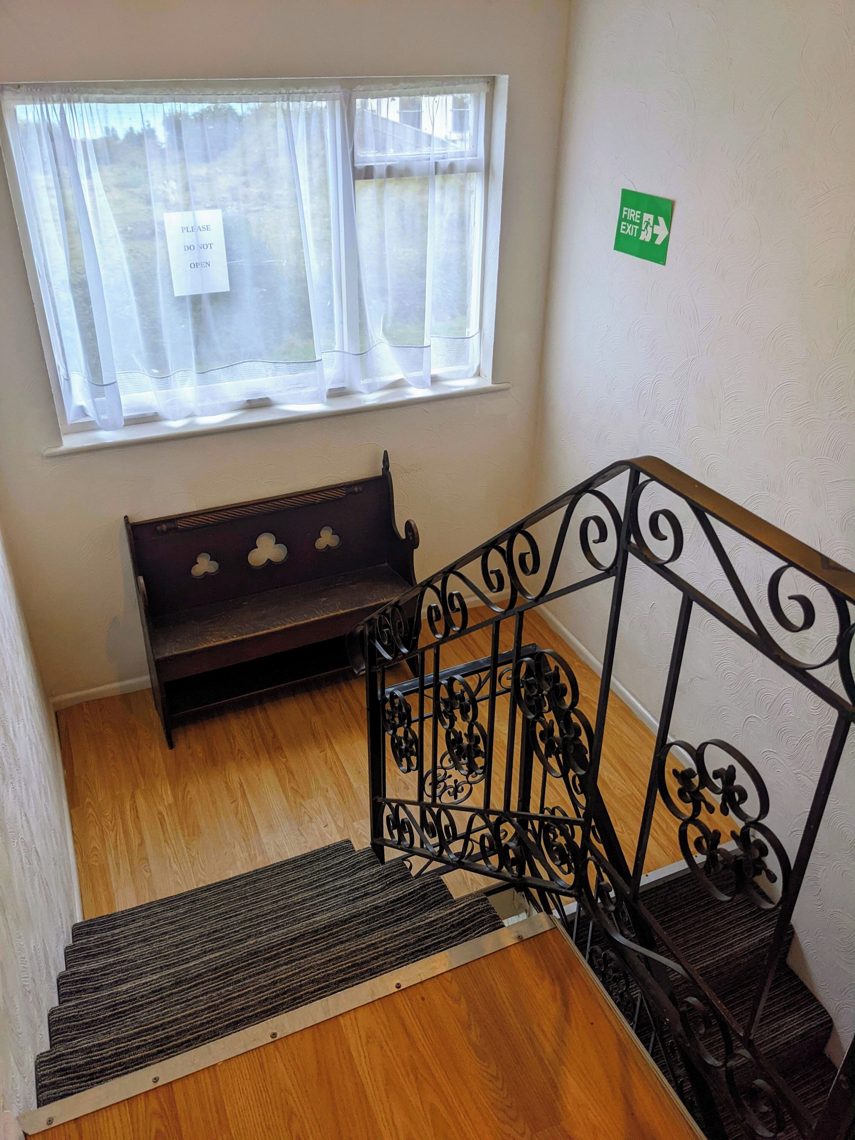 A wooden staircase with a metal handrail, a bench, and a window with a 'Please Do Not Open' sign.