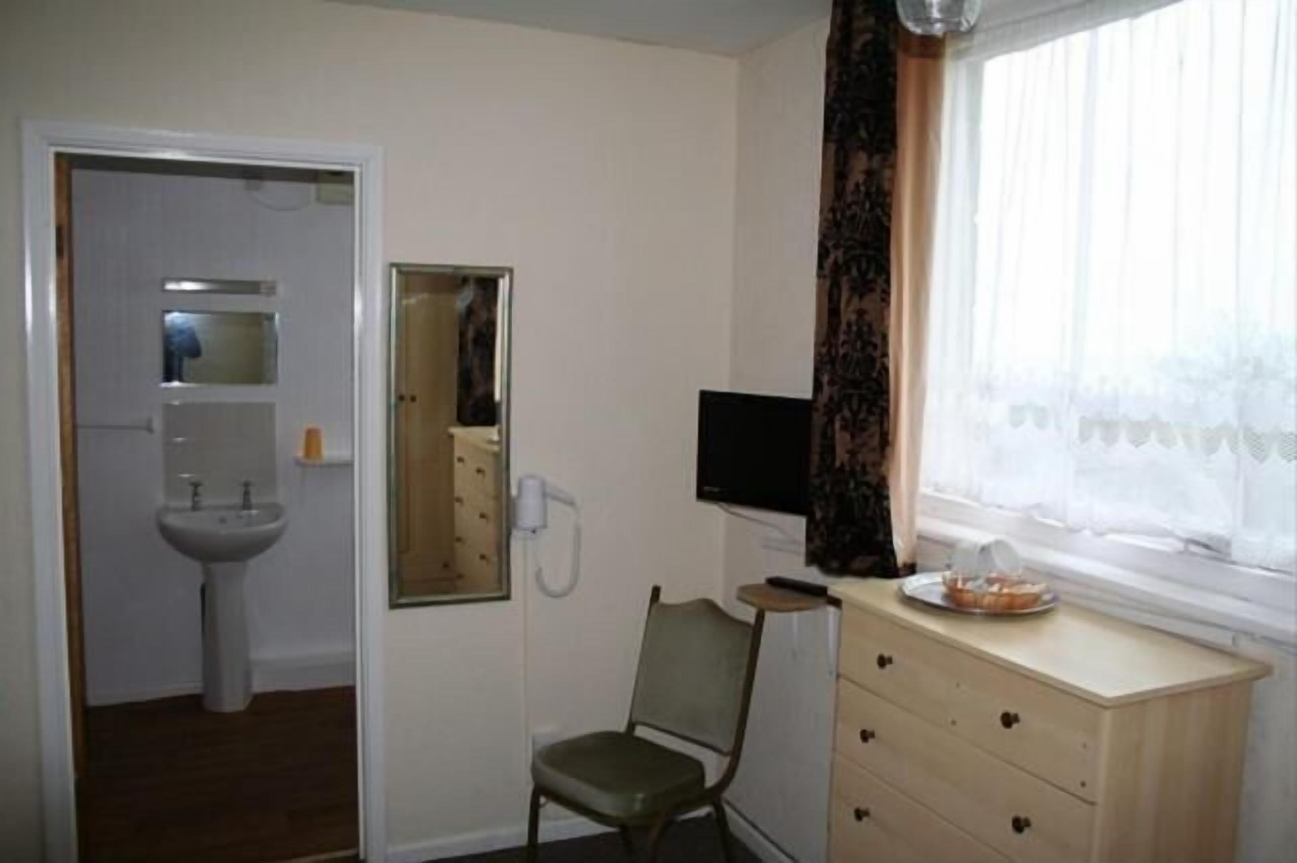A room with a sink, a chair, a television, and a window with curtains.
