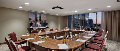 A conference room with a long table, red chairs, and a city view through large windows.