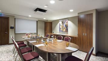 Ein Konferenzraum mit langem Tisch, Stühlen, einer Projektionsleinwand und einem großen Gemälde an der Wand.