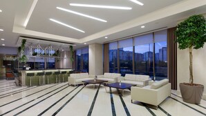 A modern lobby with a seating area, large windows, and a potted tree. - Hilton Garden Inn Istanbul Beylikduzu (Istanbul)