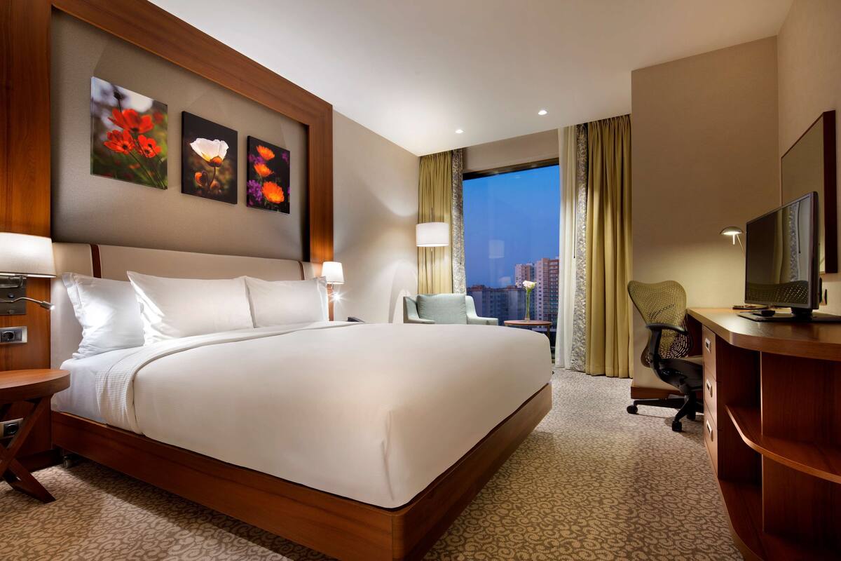 A hotel room with a large bed, a desk, a chair, and a television.