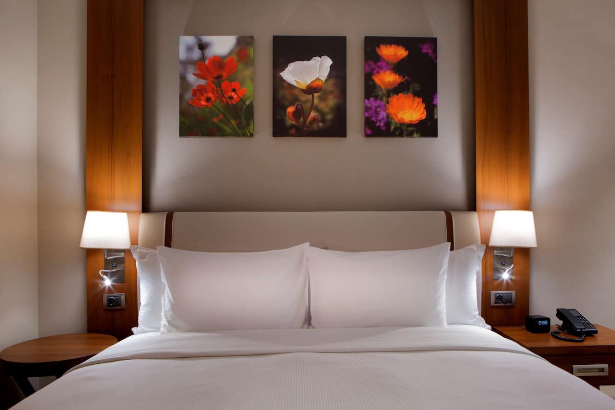 A hotel room with a large bed, two bedside tables with lamps, and three framed floral paintings on the wall.