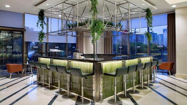 A modern bar area with a central bar, multiple stools, and hanging greenery. - Hilton Garden Inn Istanbul Beylikduzu (Istanbul)