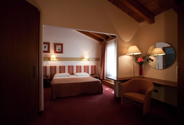 A hotel room with a bed, a chair, a desk, a mirror, and two wall-mounted lamps. - Eurohotel Palace Maniago (Maniago)
