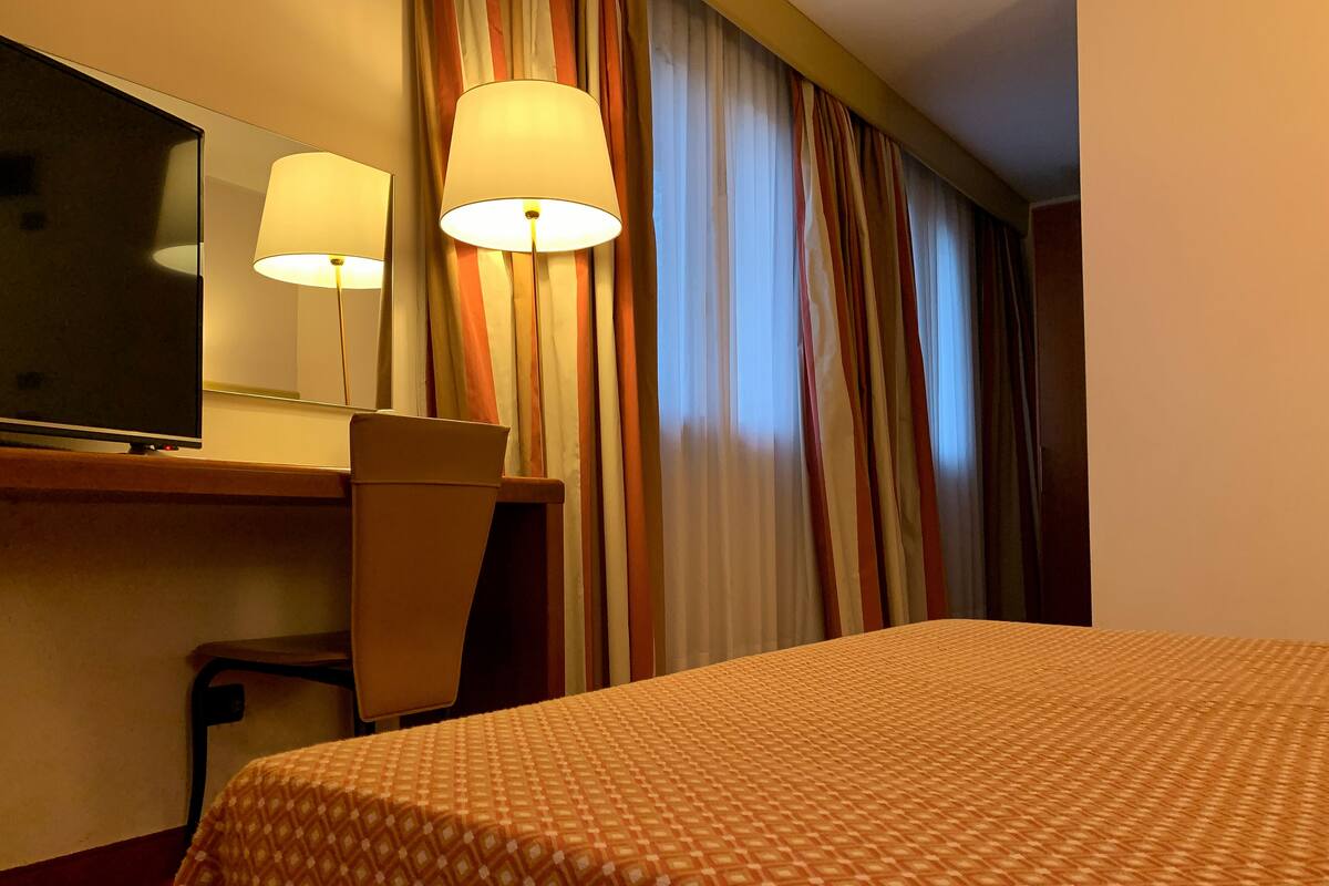 Habitación de hotel con cama, escritorio con silla, lámpara y un espejo grande.