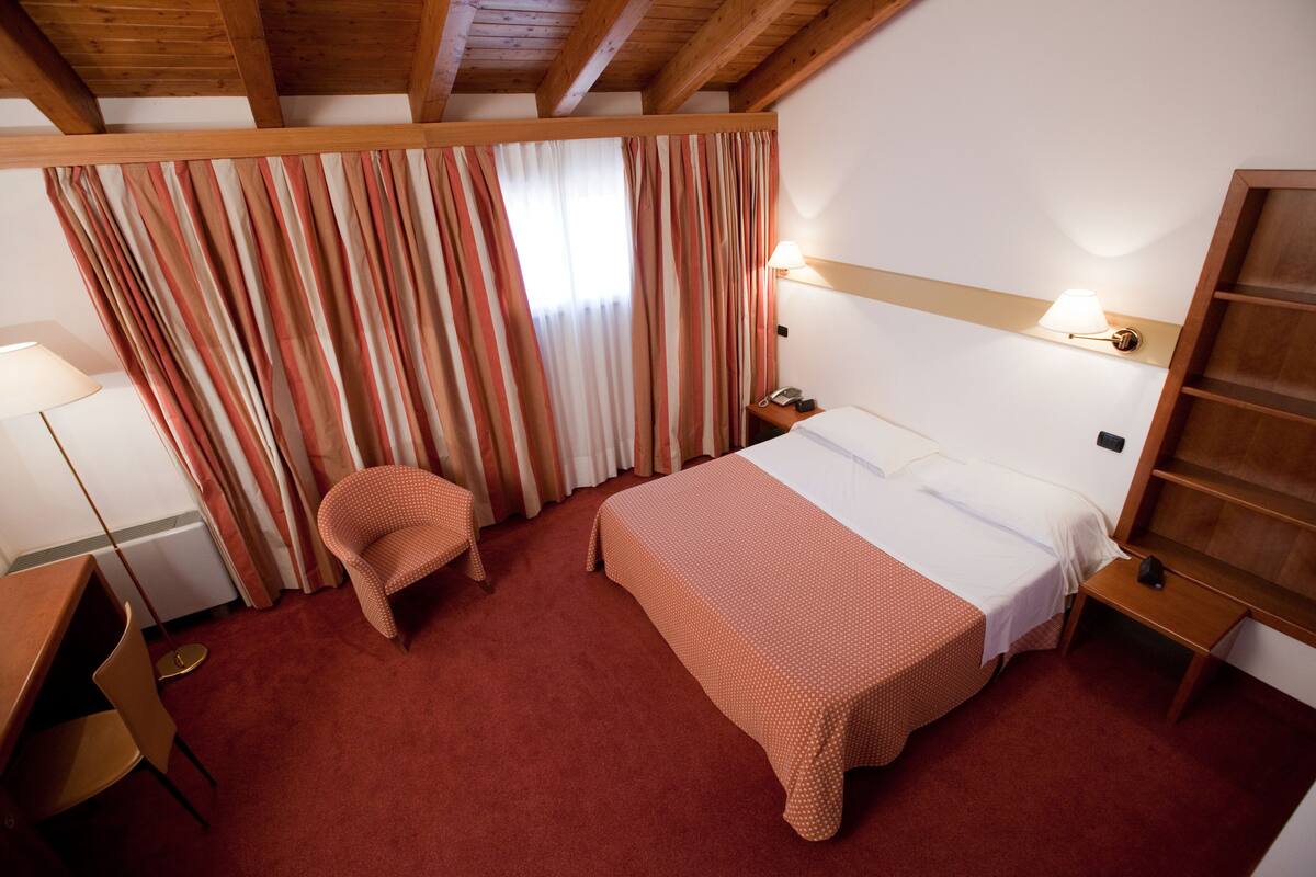Una habitación de hotel con una cama, una silla, un escritorio y una lámpara.