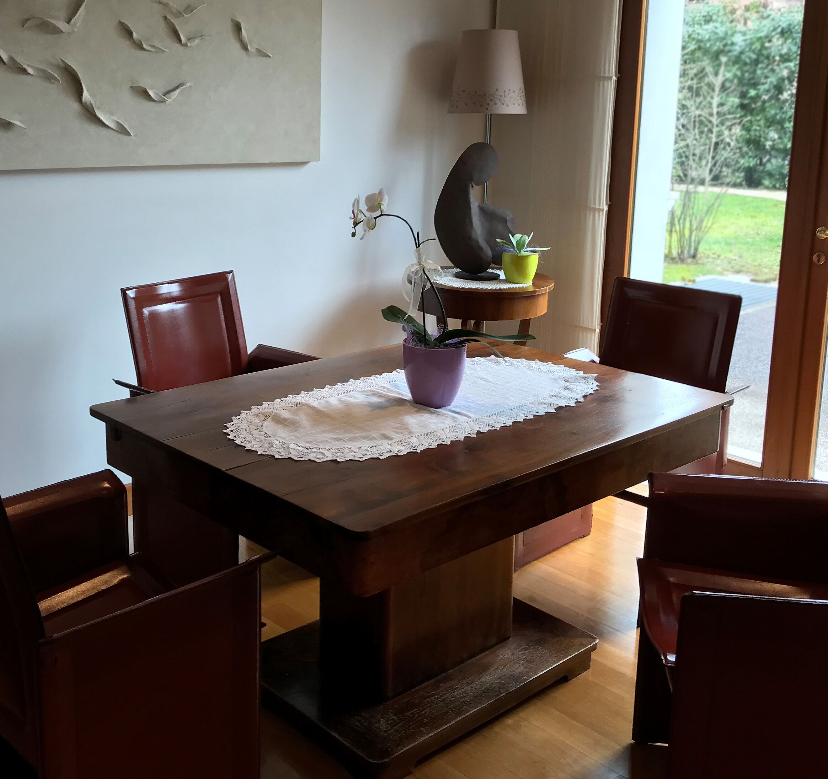 A dining table with a lace tablecloth, surrounded by four chairs, and a potted plant on the table.