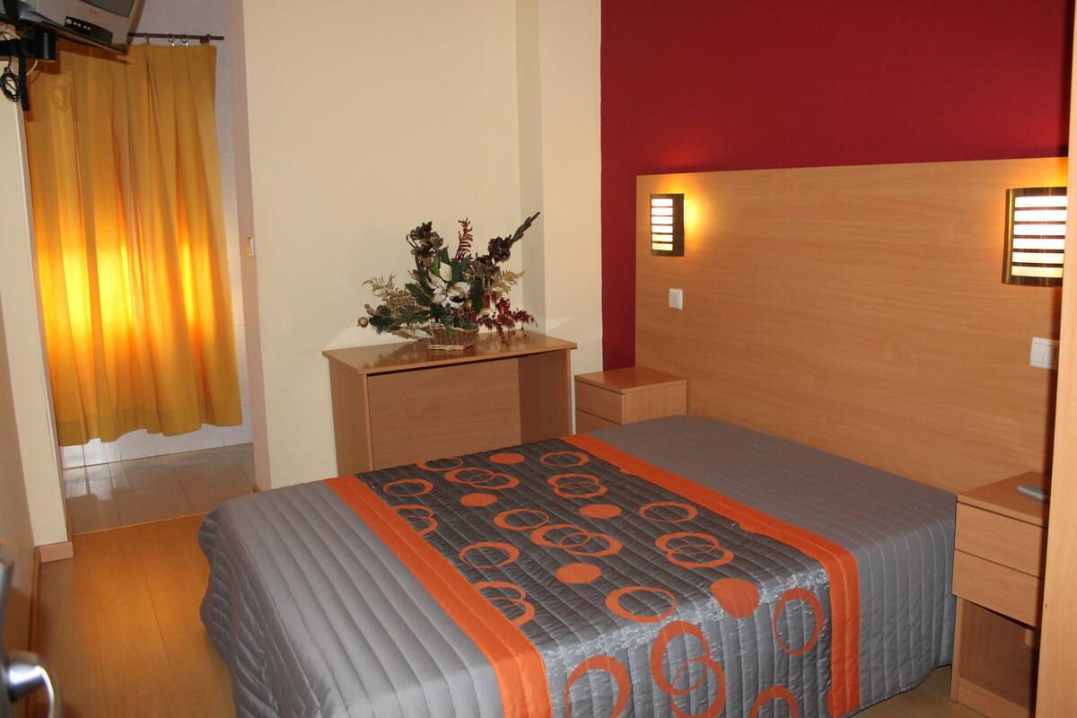 A bedroom with a bed, a nightstand, a dresser, and a wall-mounted light.