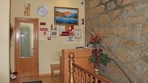 A reception area with a wooden desk, a clock, a painting, and a stone wall. - Guest House Estrela (Porto)
