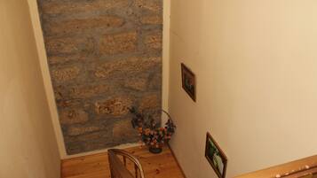 Una escalera con barandillas de madera, pared de piedra y un florero con flores.