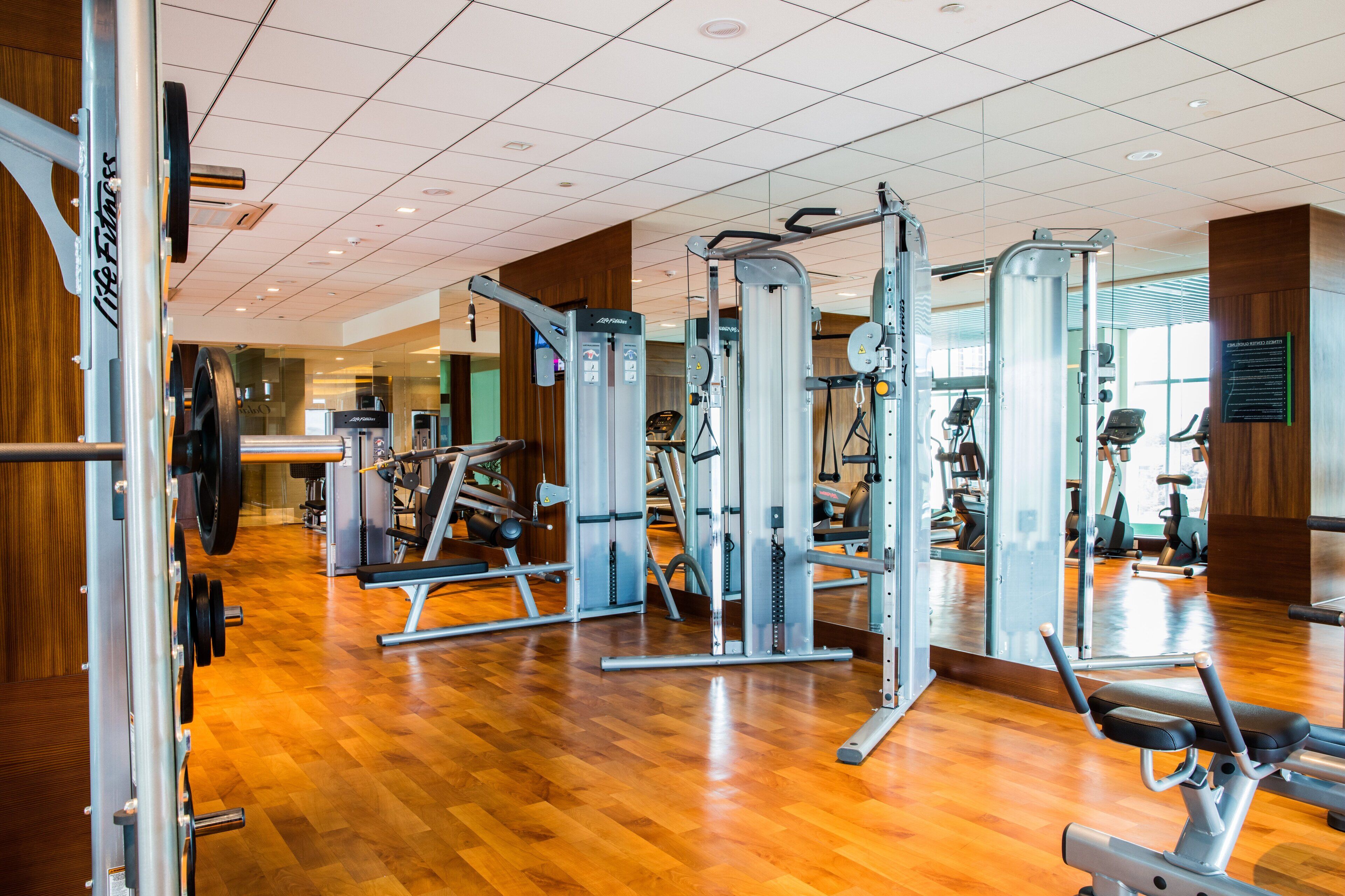 Un gimnasio con diversas máquinas de ejercicio, suelo de madera y un espejo grande.