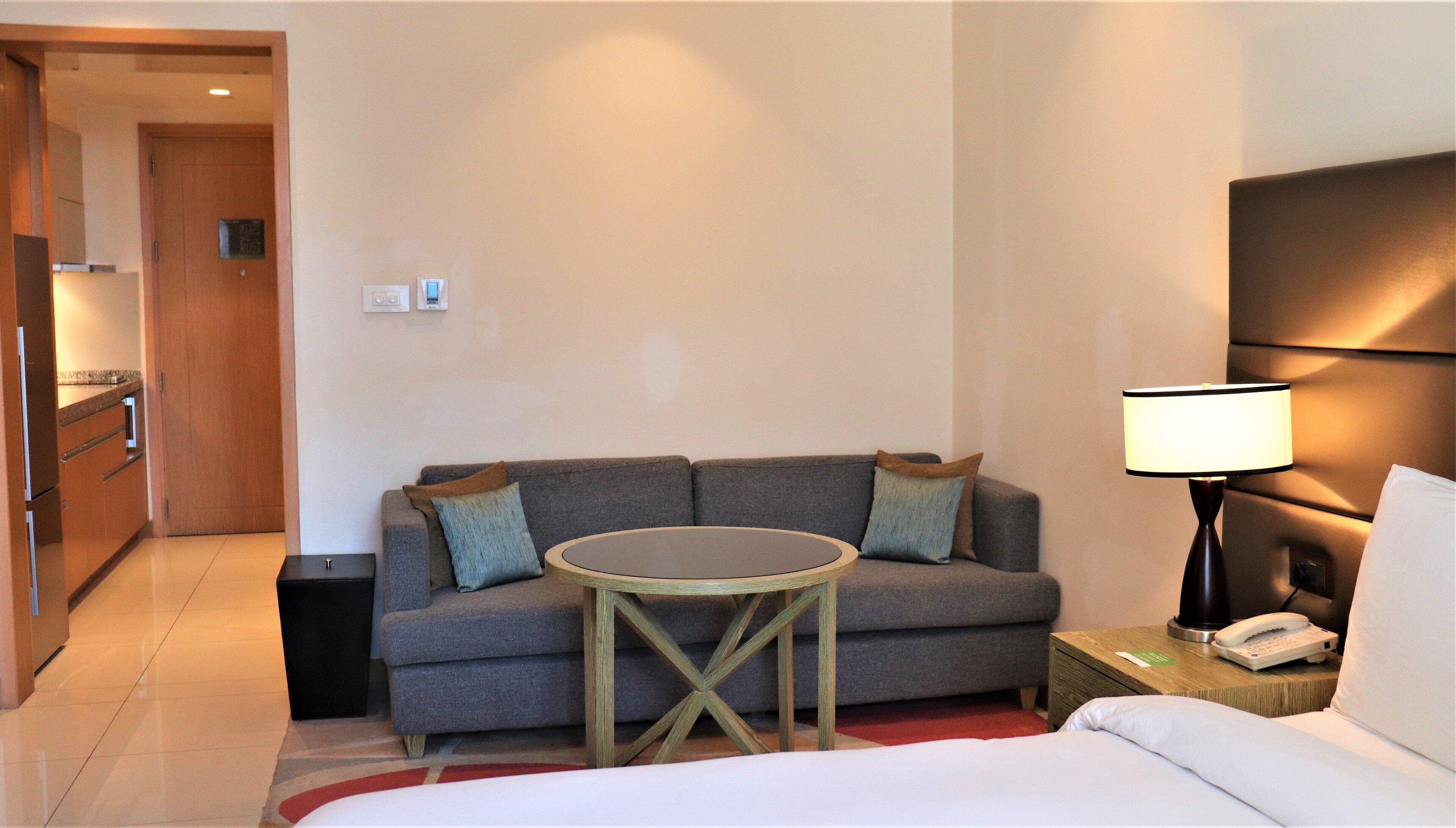 A hotel room with a bed, a sofa, a small round table, a nightstand with a lamp, and a telephone.