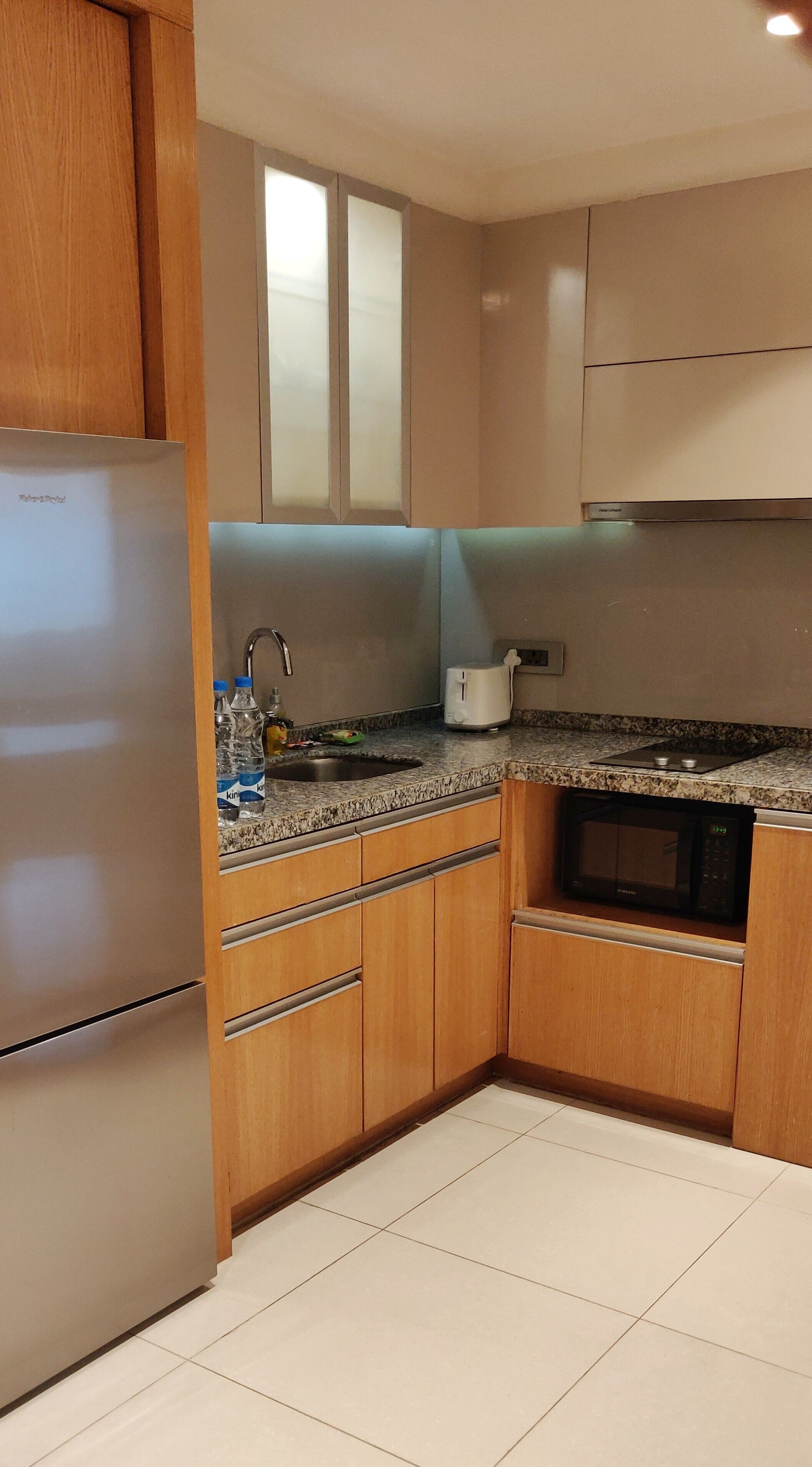 A kitchen with wooden cabinets, a stainless steel refrigerator, a granite countertop, a built-in microwave, and a sink with a faucet.