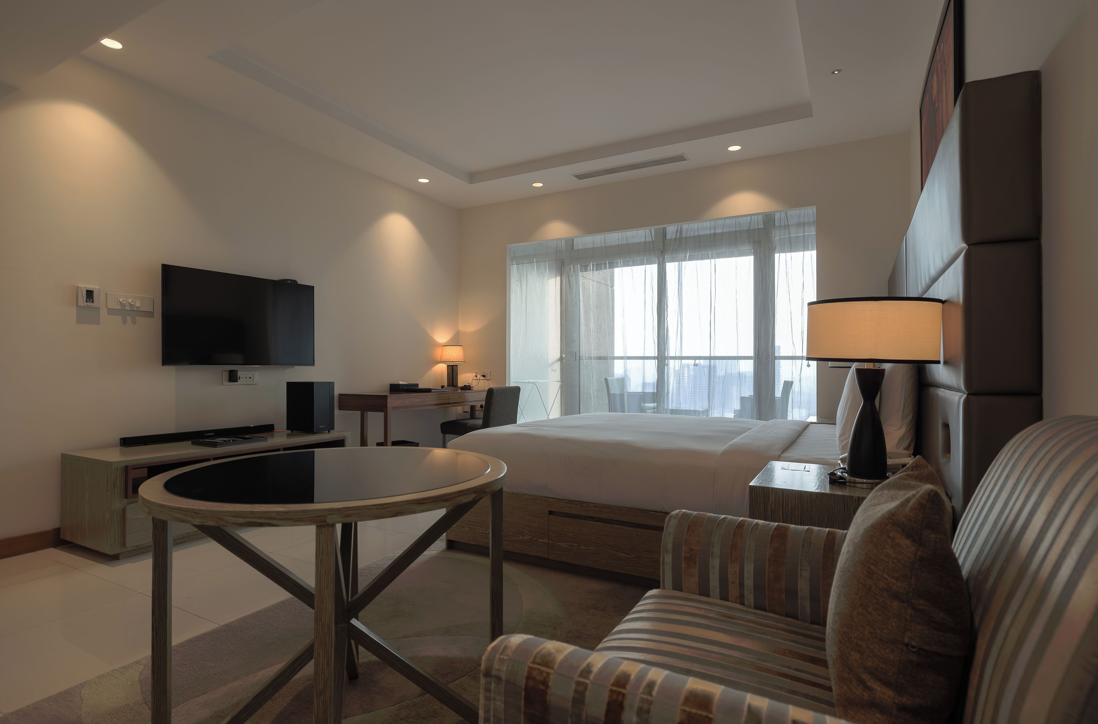 Una habitación de hotel moderna con cama, televisor, escritorio, silla y lámpara.