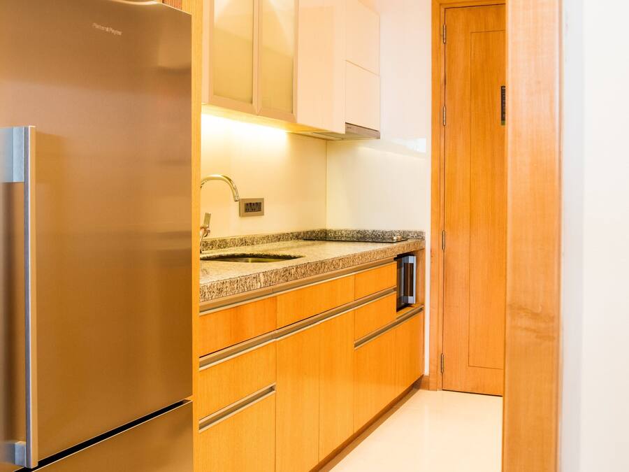 A modern kitchen with wooden cabinets, a stainless steel refrigerator, and a granite countertop.