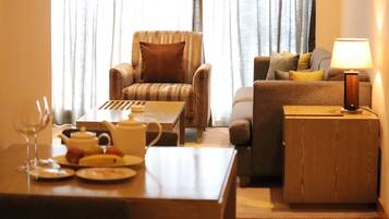 Una sala de estar con un sillón a rayas, un sofá con cojines, una mesita de madera con una lámpara y una mesa de comedor con platos y una tetera.