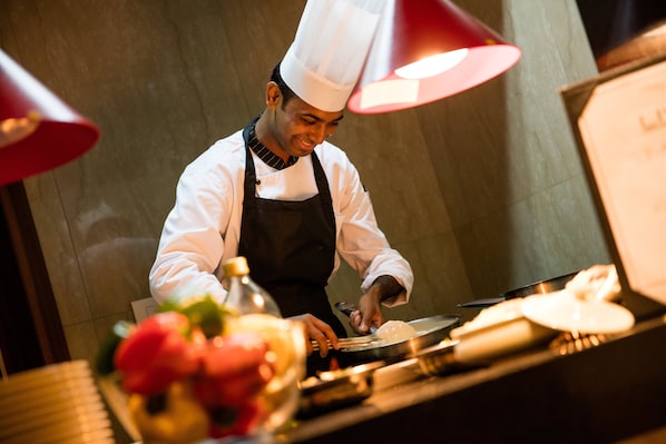 Un chef con uniforme y gorro blancos preparando comida en una barra con una lámpara roja sobre ella.