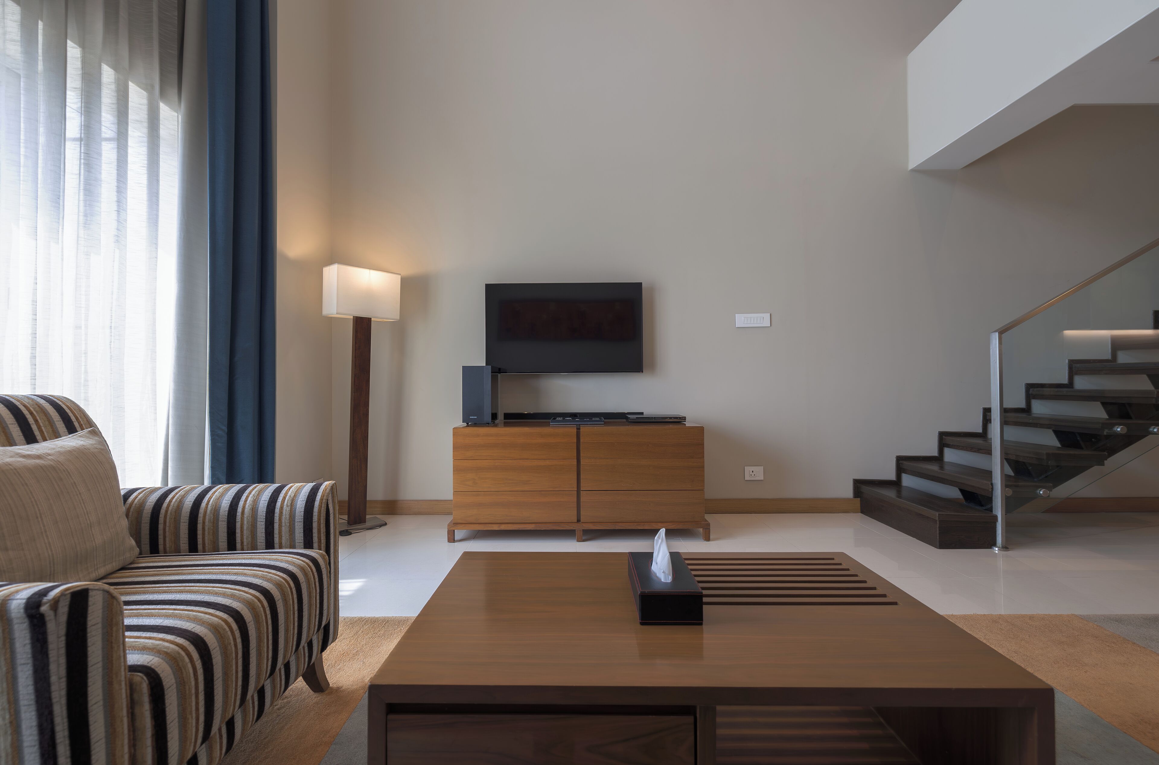 A modern living room with a sofa, a coffee table, a TV on a wooden cabinet, and a staircase.