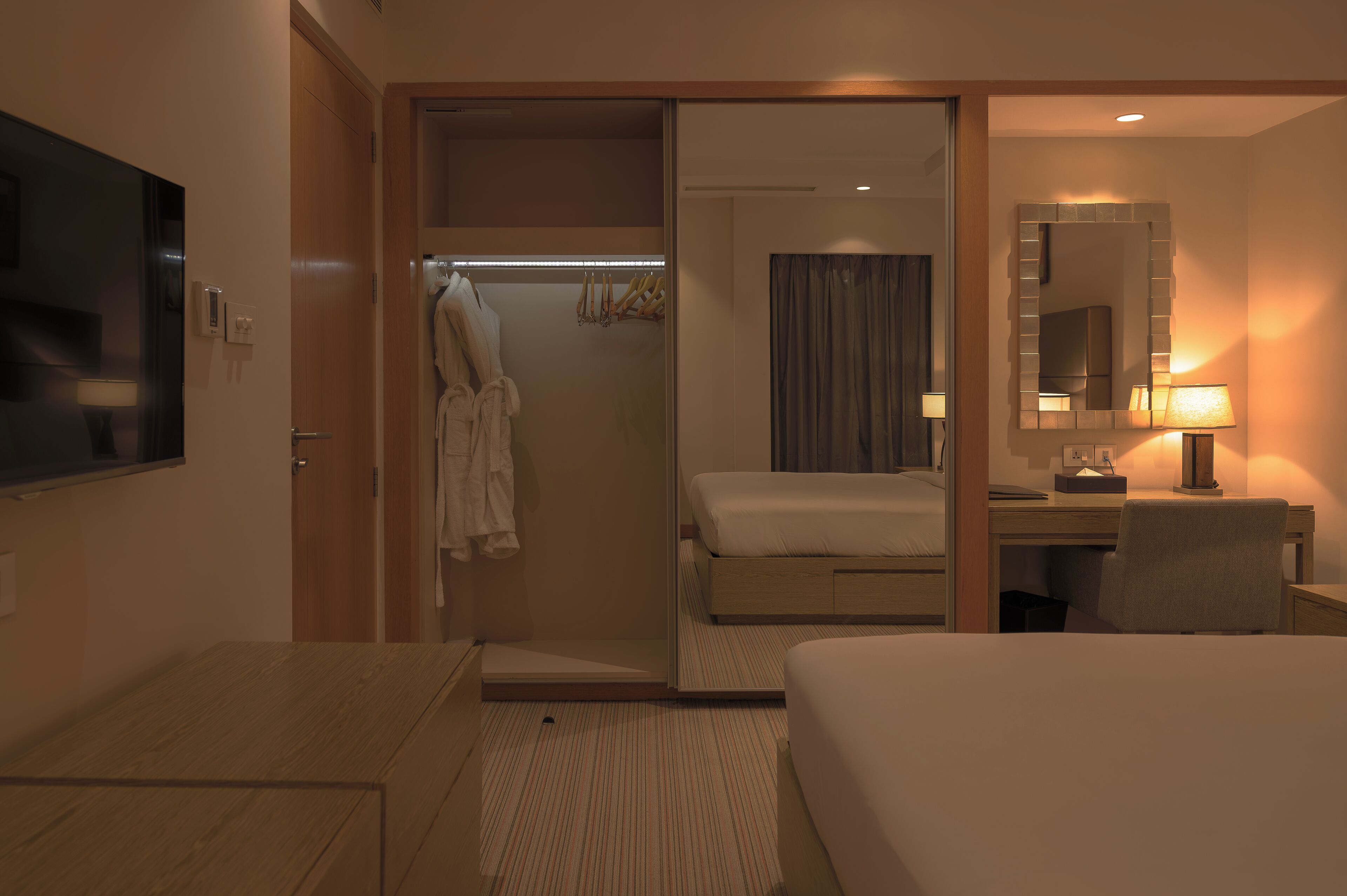 Habitación de hotel con cama, escritorio, silla, televisor, espejo y zona de ducha.