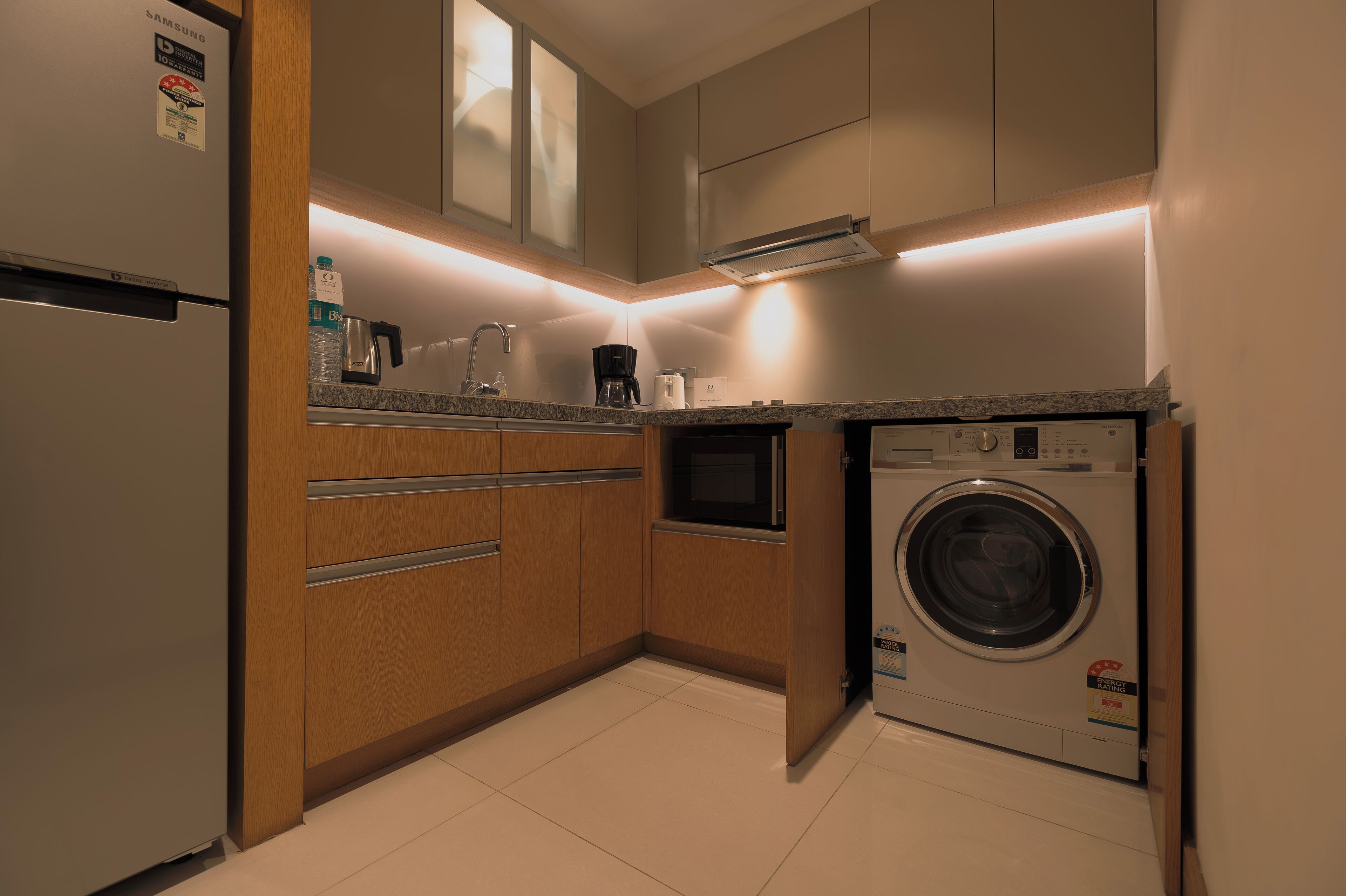 A compact kitchen with a built-in washer and dryer, wooden cabinets, and a stainless steel refrigerator.