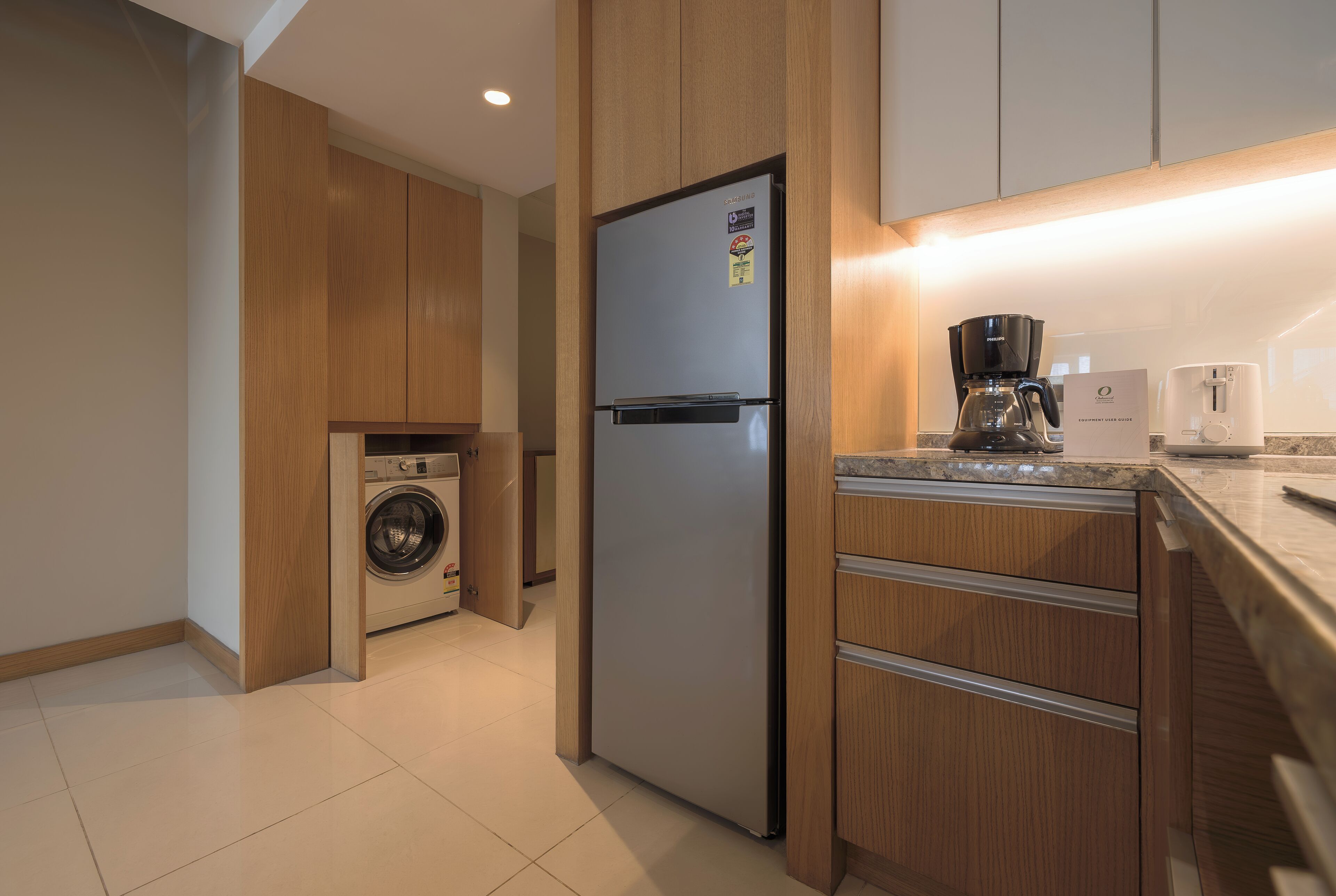 Una cocina moderna con armarios de madera, un refrigerador de acero inoxidable, lavadora, cafetera y tostadora.