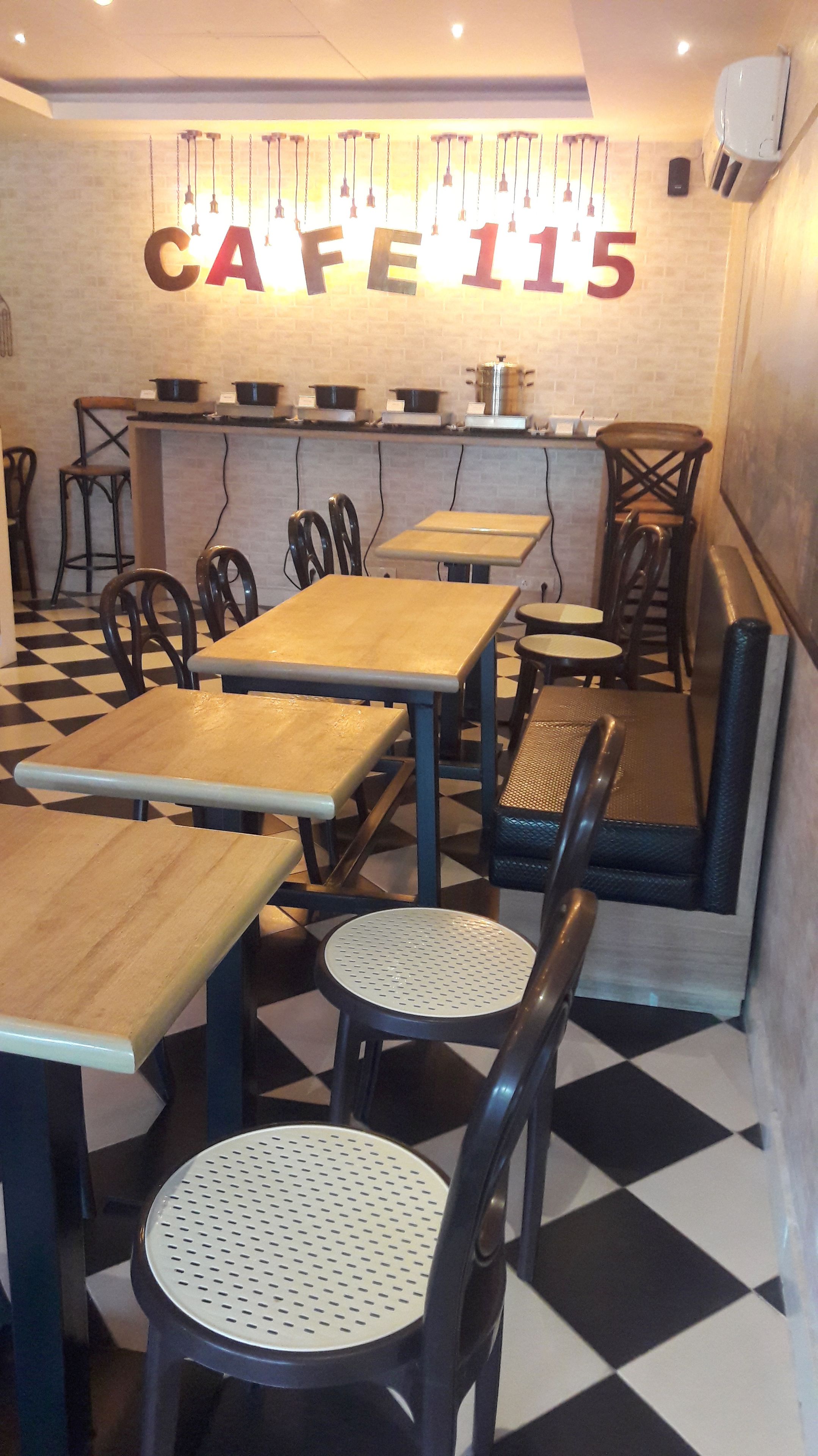 A cafe interior with tables and chairs, a black and white checkered floor, and a wall with the text "CAFE 115".