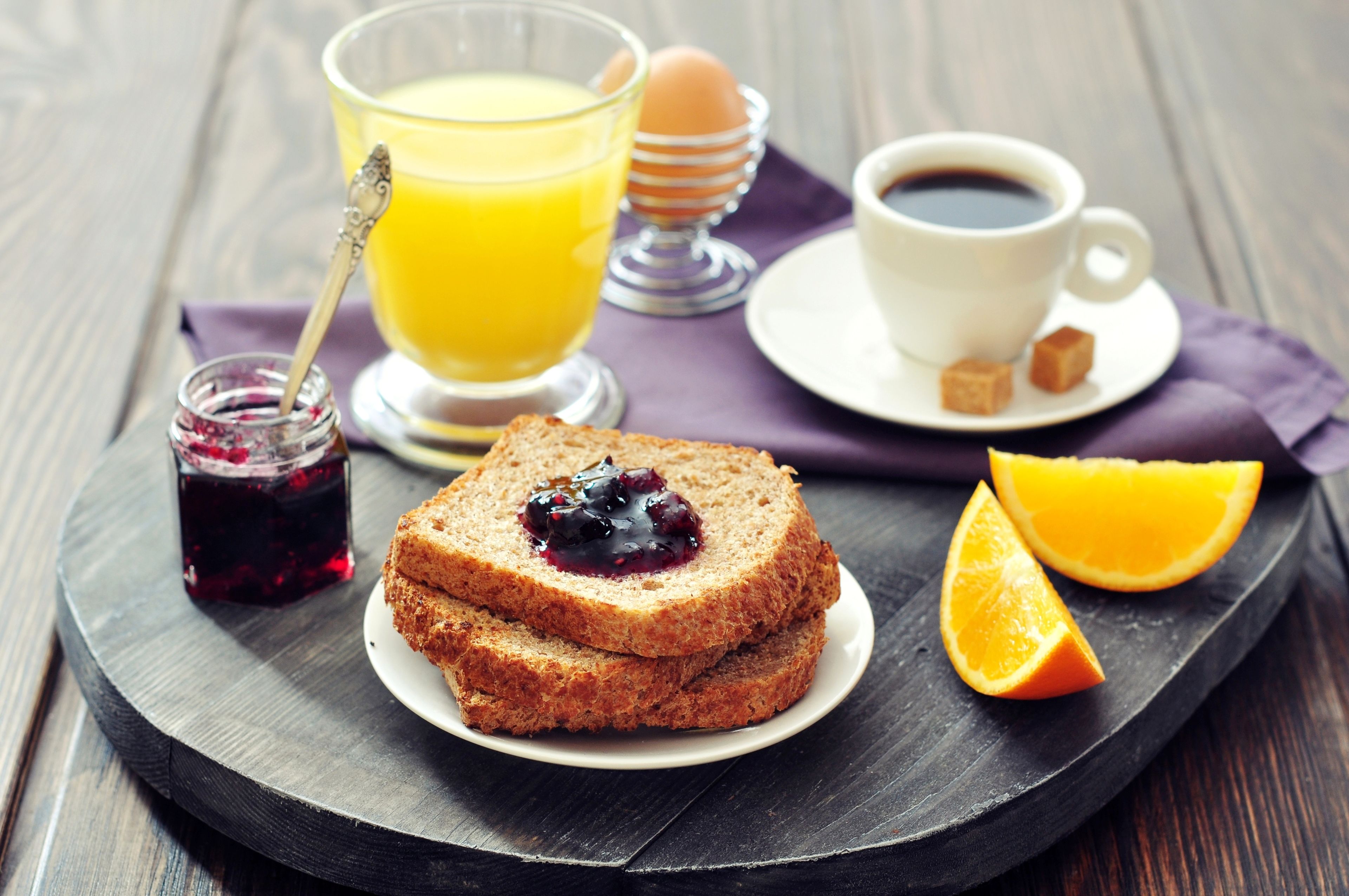 A breakfast tray with toast, jam, orange juice, coffee, and a small jar of jam.