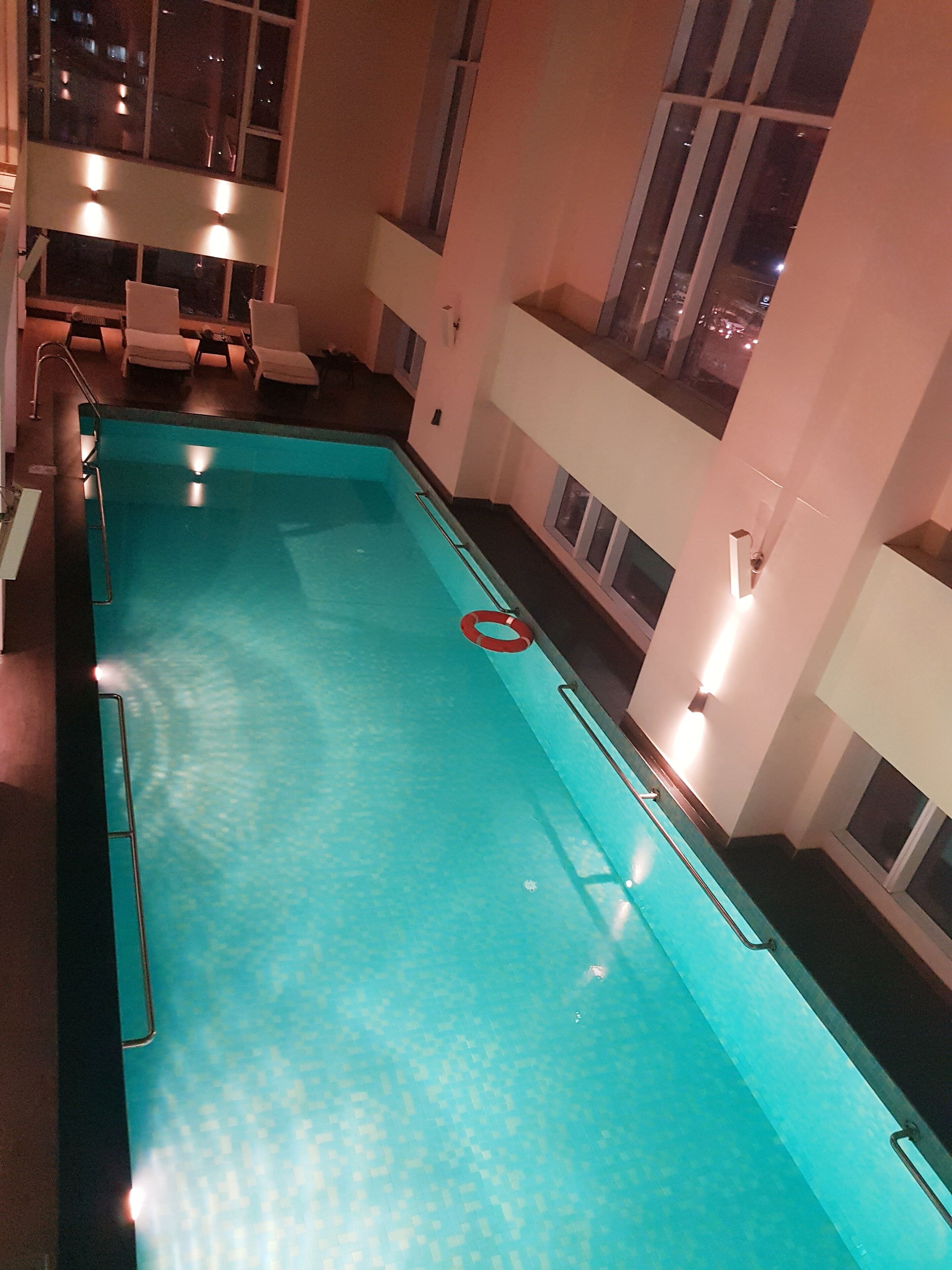 An indoor swimming pool with clear water, a lifeguard chair, and a red safety ring.