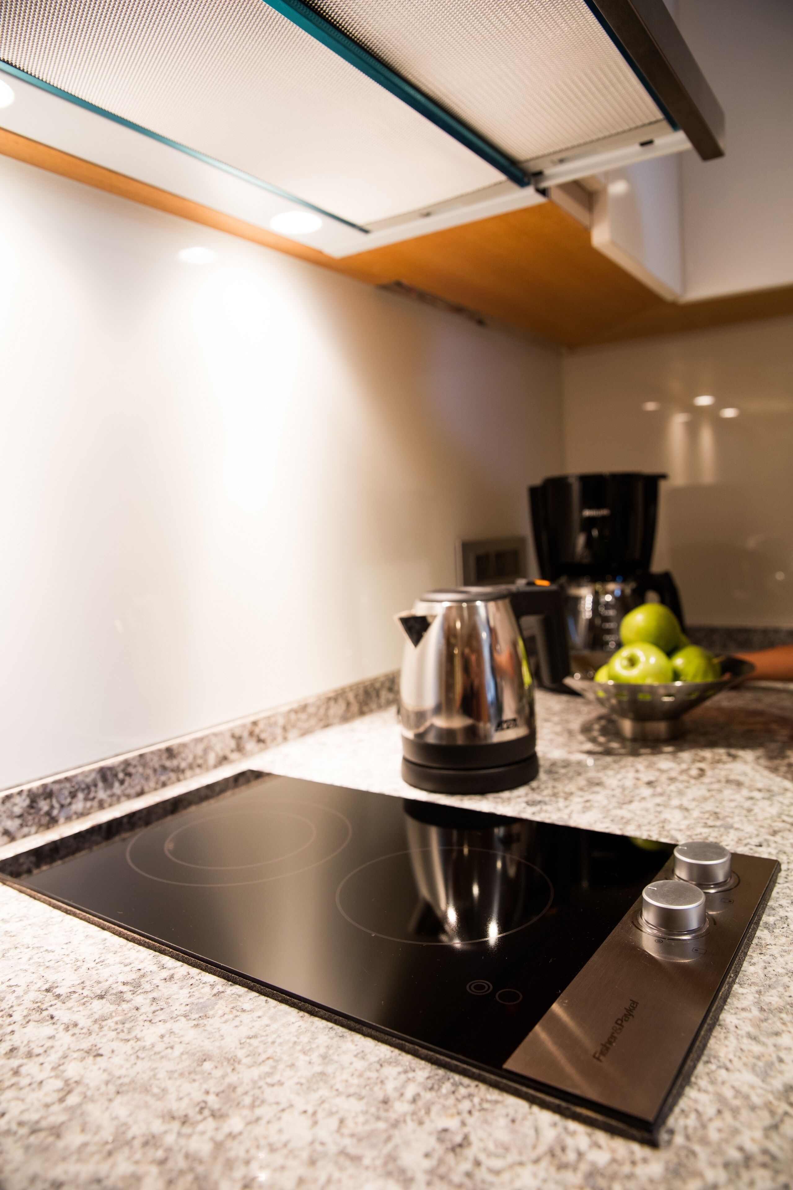 A kitchen with a black induction cooktop, a kettle, and a bowl of green apples on the counter.