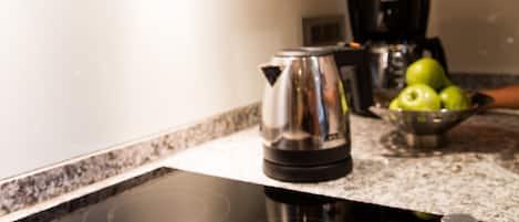 Una cocina con una placa de inducción negra, un hervidor y un bol con manzanas verdes sobre la encimera.