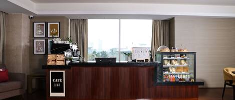 Un vestíbulo de hotel moderno con mostrador de recepción, obras de arte enmarcadas, una estación de café y vistas a la ciudad.