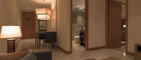 Habitación de hotel con piso de madera, sofá, una mesa y una lámpara. Se ve un baño a través de una puerta abierta.