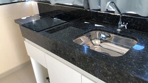 A kitchen with a black granite countertop, stainless steel sink, and white cabinetry. - Lagoinha Beach Residencial (Bombinhas)