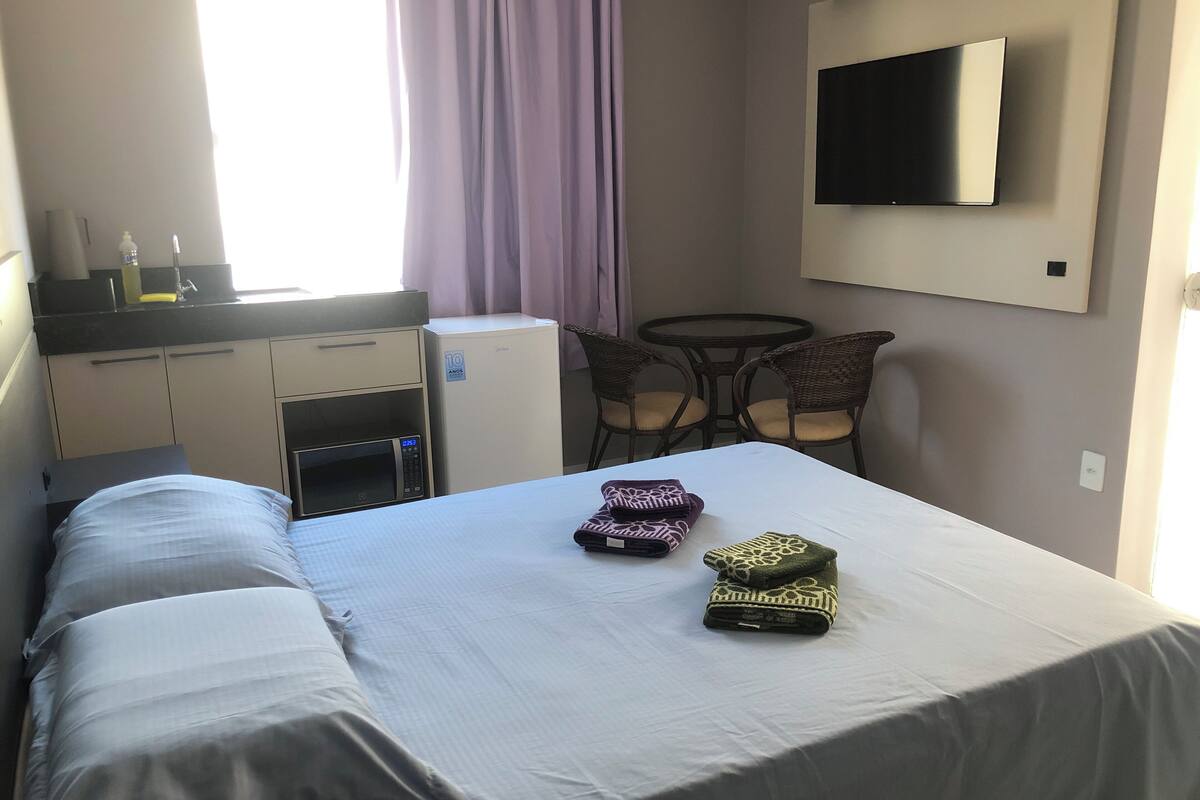 A hotel room with a bed, a desk, a microwave, a refrigerator, a TV, and two chairs.