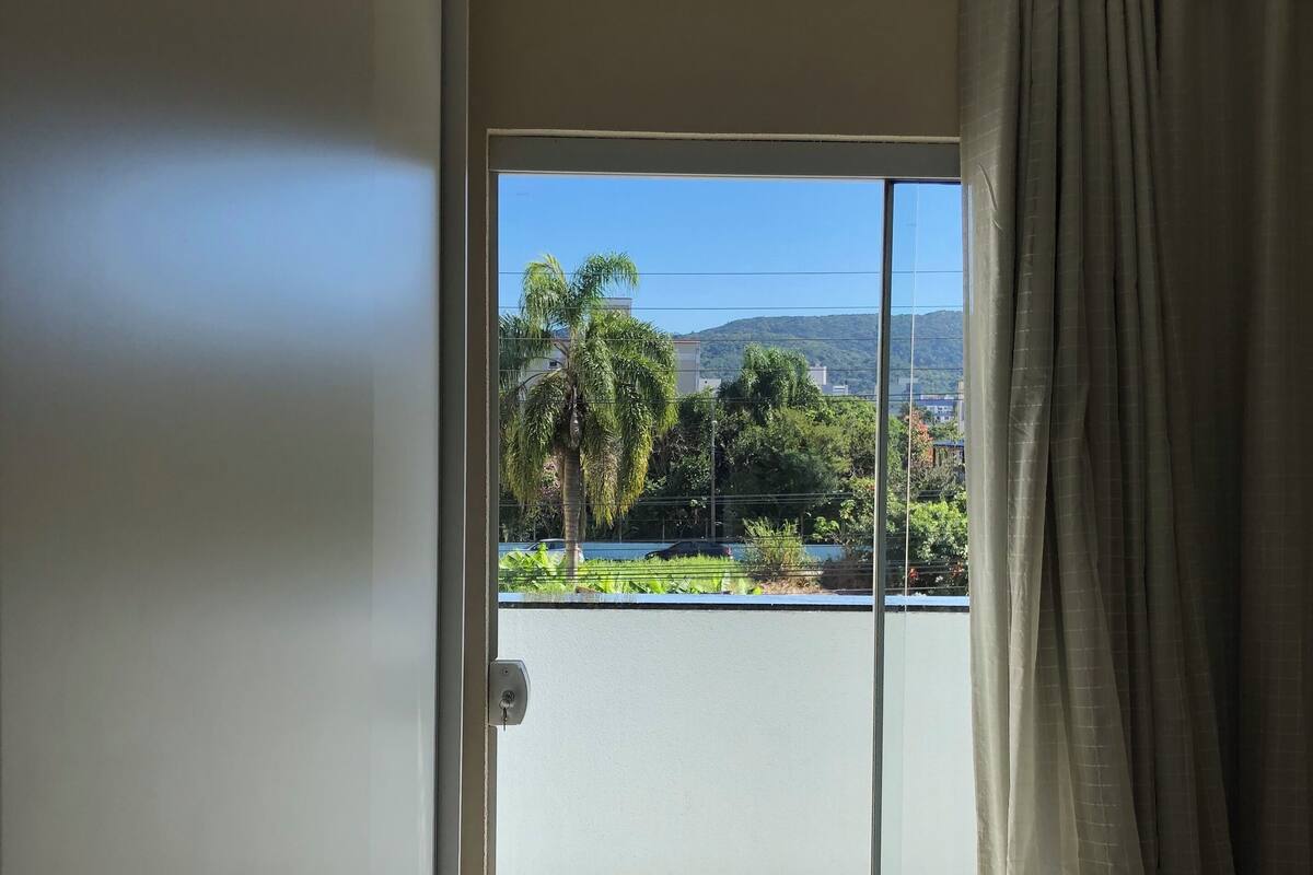 A room with a sliding glass door leading to a balcony with a view of greenery and buildings.