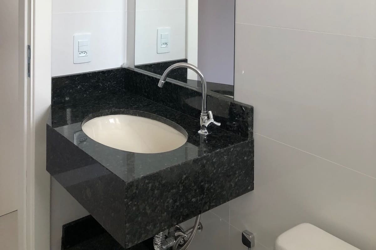 A modern bathroom with a white sink, black countertop, and a large mirror.