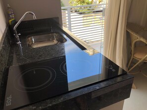 A kitchen with a black induction cooktop, a sink, and a bottle of hand soap.